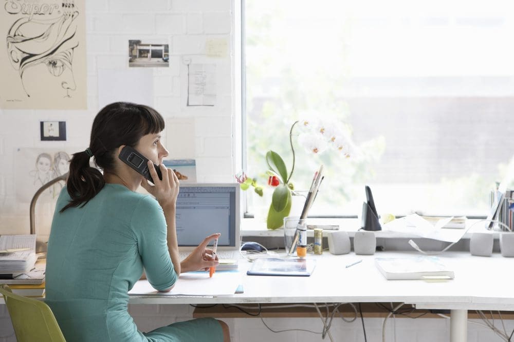 Young,Female,Artist,Using,Cell,Phone,At,Desk